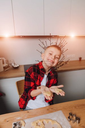 Foto de Un niño pequeño en una mesa de madera en la cocina haciendo galletas con cortador de galletas en una forma de duro. Vista frontal - Imagen libre de derechos