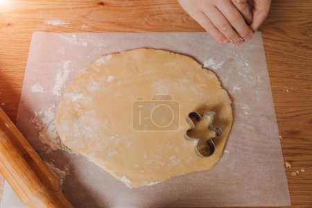 Foto de Cierre las manos de los niños en una mesa de madera en la cocina haciendo galletas con cortador de galletas en forma de hombrecito. Vista superior - Imagen libre de derechos