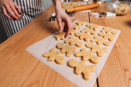 Foto de Cierre las manos de las mujeres en una mesa de madera en la cocina haciendo galletas con cortador de galletas en forma de hombrecito y estrellas. Vista superior - Imagen libre de derechos