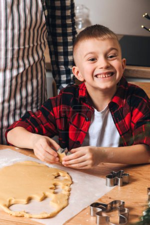 Foto de Papá e hijo en una mesa de madera en la cocina haciendo galletas con cortador de galletas en forma de hombrecito. Vista frontal - Imagen libre de derechos