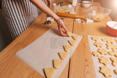 Foto de Cierre las manos de las mujeres exponen las galletas formadas en forma de corazón en una bandeja para hornear en una mesa de madera en la cocina. Cocinar postres en casa. Vista superior - Imagen libre de derechos