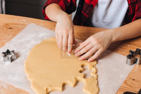 Foto de Niño en una mesa de madera en la cocina haciendo galletas con cortador de galletas en forma de hombrecito. Vista frontal - Imagen libre de derechos
