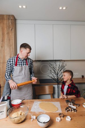 Foto de Papá e hijo en una mesa de madera en la cocina haciendo galletas, harina moldeada. Vista frontal - Imagen libre de derechos