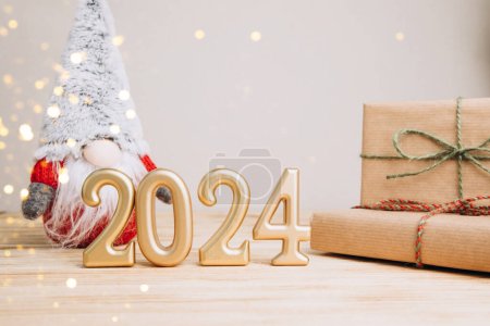 Background for greetings with empty space. Happy new year card. Figures 2024 on a light wooden background with Christmas gnome. Front view