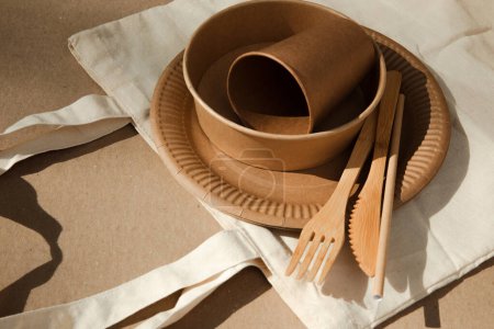 Téléchargez les photos : Ensemble d'ustensiles en papier et couverts en bois dans un sac en tissu sur fond marron. Concept écologique, zéro déchet. Vue du dessus - en image libre de droit
