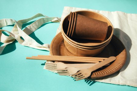 Téléchargez les photos : Des ustensiles en papier, des assiettes et des couverts en bois sur un sac textile sur fond bleu. Modèle écologique, concept zéro déchet. Vue du dessus - en image libre de droit