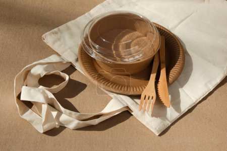 Téléchargez les photos : Ensemble d'ustensiles en papier et couverts en bois dans un sac en tissu sur fond marron. Concept écologique, zéro déchet. Vue du dessus - en image libre de droit
