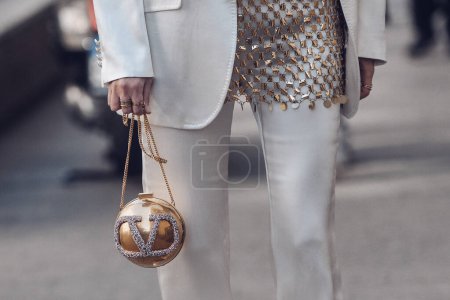 Téléchargez les photos : Milan, Italy - February 25, 2022: Crop anonymous female in trendy outfit carrying round golden ball bag on blurred background of street. - en image libre de droit