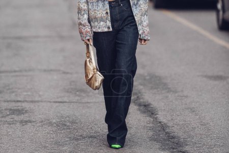 Téléchargez les photos : Milan, Italy - February 25, 2022: Female in jeans and crop top with ornamental jacket and stylish bag walking on city street of Milan. - en image libre de droit
