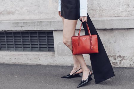 Photo for Milan, Italy - February 24, 2022: Woman in black dress with white sleeves wearing unusual pointy toe shoes walking on street with red handbag. - Royalty Free Image