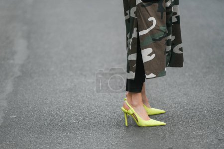 Foto de Milan, Italy - February 24, 2022: Woman in long dress with camouflage print pants and high heeled yellow shoes standing on pavement during fashion week - Imagen libre de derechos