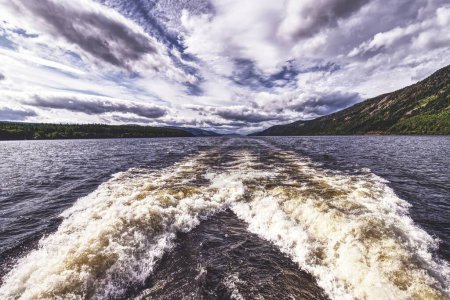 Photo for Experience the exhilarating sensation of speed and adventure with this striking top-view photograph of a fast-moving ship trail on Loch Ness. The image captures a white, foamy wave trailing behind - Royalty Free Image