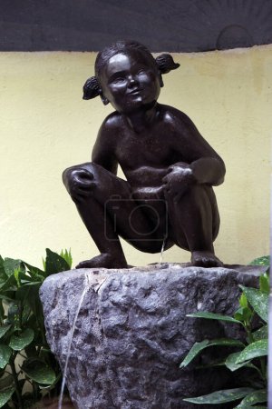 Pee belga famosoEsta imagen muestra la estatua icónica de una chica que orina, una contraparte menos conocida pero igualmente intrigante del famoso Manneken Pis de Bruselas. Situado en un entorno de jardín, la estatua