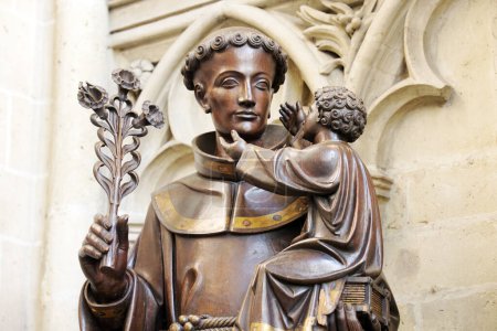 Foto de Esta fotografía captura la solemne belleza de una estatua de bronce dentro de la catedral de Gante, retratada en tonos ricos y cálidos. La figura santa, con expresión facial serena, sostiene a un niño y a un lirio - Imagen libre de derechos
