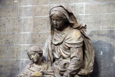 Foto de Esta evocadora imagen captura una escultura de piedra de una madre y un niño, situada dentro de los solemnes confines de la Catedral de Gante. La madre, representada con túnicas que fluyen, mira al niño con una - Imagen libre de derechos