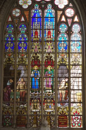 Foto de Esta impresionante imagen vertical presenta la cautivadora obra de vidrieras de la Catedral de Gante, una verdadera representación del esplendor gótico. El alto cristal de la ventana está lleno de una serie de historias representadas - Imagen libre de derechos