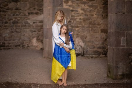 Téléchargez les photos : Mère couvre fille avec drapeau ukrainien contre vieux mur. - en image libre de droit