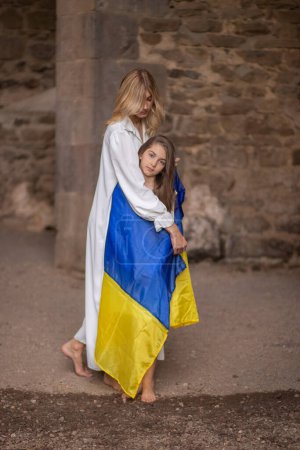 Téléchargez les photos : Mère couvre fille avec drapeau ukrainien contre vieux mur. - en image libre de droit