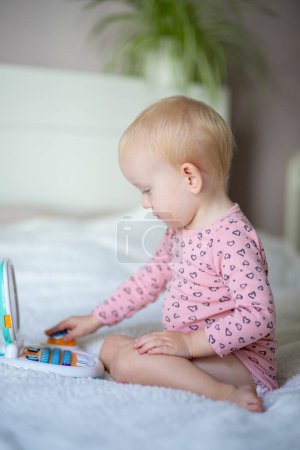 Toddler playing with a toy laptop on a bed with a plant in the background