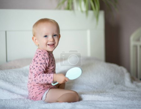 Toddler smiling holding a hairbrush sitting on a bed