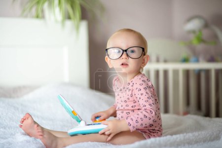 Niño pequeño con gafas jugando con un juguete educativo en una cama