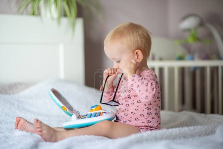 Toddler with glasses playing with an educational toy on a bed