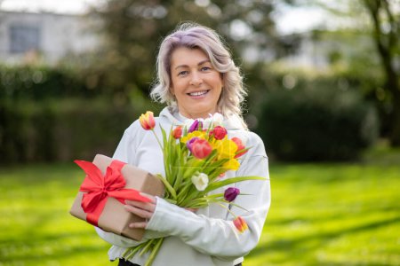 Joyeux sourire femme de 50 ans avec des tulipes et un cadeau.