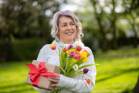 Joyeux sourire femme de 50 ans avec des tulipes et un cadeau.