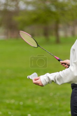 Hand with badminton racket and shuttlecock on green lawn background