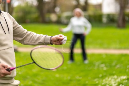 Man and woman playing badminton outdoors, focus on hand with shuttlecock.