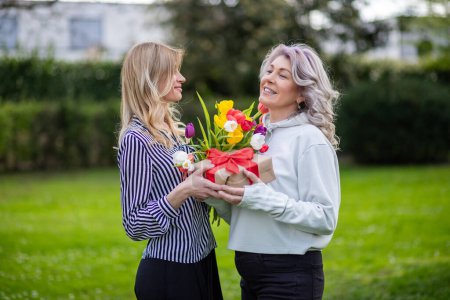 Madre e hija sonriendo con regalo y tulipanes