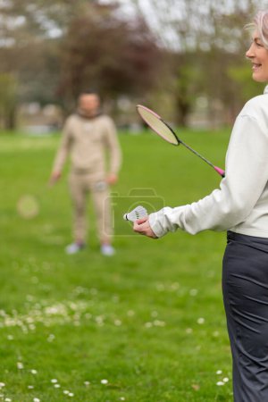 Woman playing badminton outdoors, man in distance.