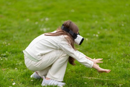 Girl in virtual reality headset reaching out in a park.