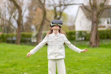 Girl in virtual reality with arms outstretched in a park.