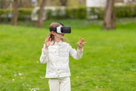 Girl in virtual reality headset with arms outstretched in a park.