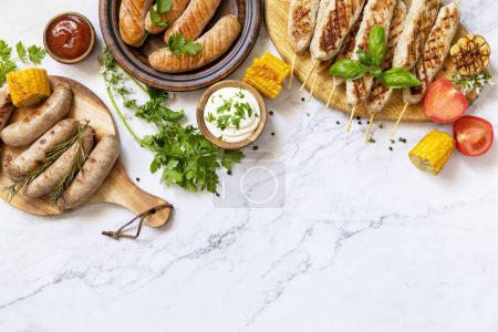 Foto de Grill food menu. Various bbq grilled sausages with fresh herbs and spices on marble tabletop. Summer party food. View from above. Copy space. - Imagen libre de derechos