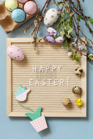 Téléchargez les photos : Springtime welcome concept. Letter Board Quote HAPPY EASTER in letter board Easter eggs and green branches on a blue background, minimalism style composition. - en image libre de droit