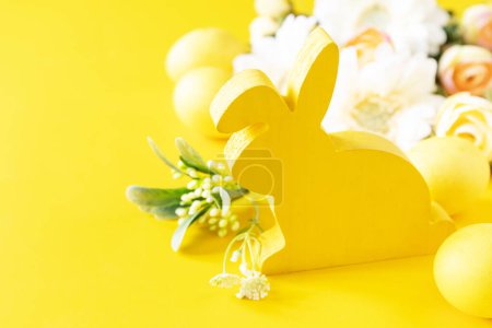 Photo for Easter composition with colorful eggs, wooden bunny and spring flowers on yellow background. Copy space. - Royalty Free Image