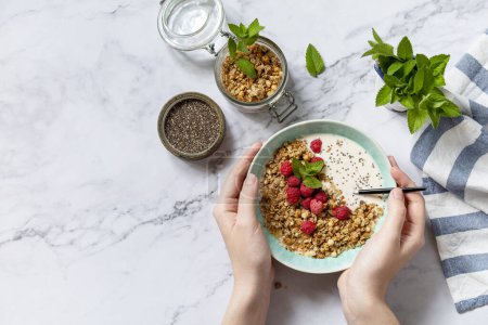 Photo for Breakfast, sweet dessert. Diet nutrition concept. Woman are cooking granola with yogurt, chia seeds and raspberry on a marble tabletop. View from above. Copy space. - Royalty Free Image