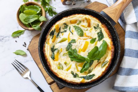 Photo for Spinach and cheese omelette. Frittata made of eggs, paprika and spinach in a frying pan on a marble countertop. - Royalty Free Image