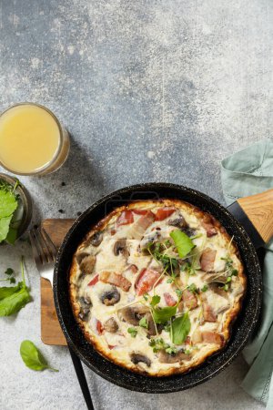 Téléchargez les photos : Petit déjeuner italien. Omelette rustique (frittata) avec champignons et bacon sur une casserole en fonte. Vue d'en haut. Espace de copie. - en image libre de droit