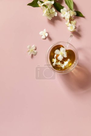 Téléchargez les photos : Tasse de thé au jasmin avec des fleurs de jasmin sur un fond rose pastel. Concept de boissons naturelles biologiques. Vue d'en haut. Espace de copie. - en image libre de droit