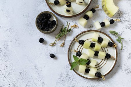 Photo for Festive summer snack of fruit and berry canapes. Vegan food. Canapes with melon and blackberries on a stone tabletop. View from above. Copy space. - Royalty Free Image