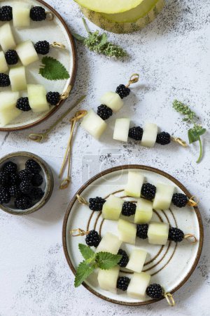 Photo for Festive summer snack of fruit and berry canapes. Vegan food. Canapes with melon and blackberries on a stone tabletop. Copy space. - Royalty Free Image