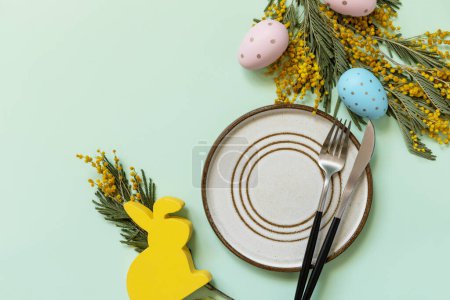 Téléchargez les photos : Table de Pâques. Assiette avec des œufs de Pâques et mimosa sur un fond vert pastel. Joyeuses vacances de Pâques concept pour les restaurants. Vue d'en haut. Espace de copie. - en image libre de droit