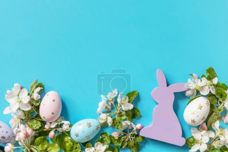 Téléchargez les photos : Composition de Pâques avec œufs colorés, lapin en bois et fleurs de printemps sur fond bleu. Concept de printemps, composition des fleurs. Carte de vœux. Vue d'en haut. Espace de copie. - en image libre de droit