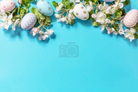 Osterkomposition mit bunten Eiern und Apfelbaumblüten auf blauem Hintergrund. Frühlingskonzept, Komposition der Blumen. Grußkarte vorhanden. Blick von oben. Kopierraum.