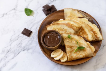 Photo for Celebrating Pancake day, healthy breakfast. Delicious homemade crepes with chocolate caramel and bananas on a marble tabletop. Copy space. - Royalty Free Image