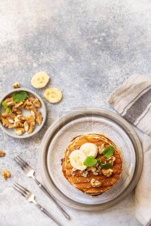 Photo for Celebrating Pancake day, american homemade breakfast. Banana gluten free pancakes with nuts and caramel on stone tabletop. View from above. Copy space. - Royalty Free Image