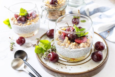 Photo for Healthy menu concept. Home made granola breakfast. Glass of parfait made of granola, berries cherry, yogurt with chia seeds on rustic table. - Royalty Free Image